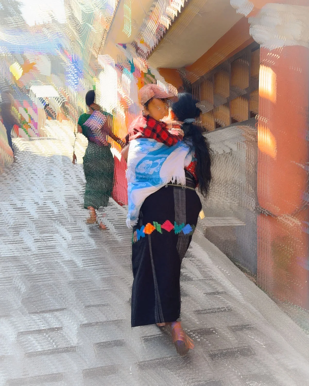 Abstract ICM Bluristic  photo - A woman carrying a child on her back walking down a street with other people in the background, with a colorful, textured visual effect.