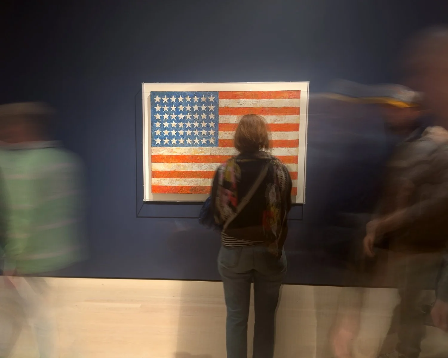 Abstract ICM Bluristic  photo - Person standing in front of an American flag artwork on a dark blue wall with blurred visitors around.