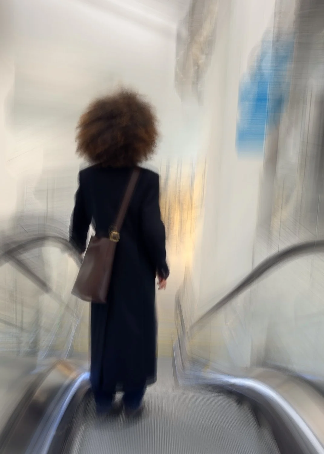 Abstract ICM Bluristic  photo - A person with large curly hair walking down an escalator, carrying a brown shoulder bag, in a modern indoor setting.