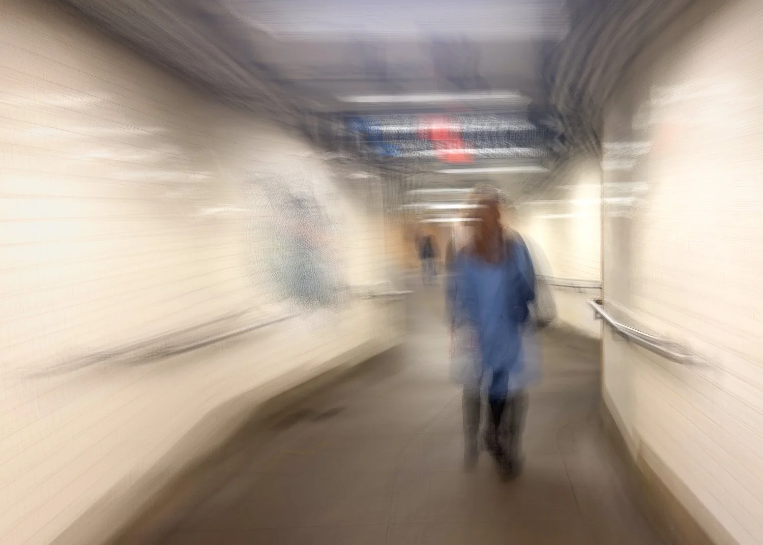 Abstract ICM Bluristic  photo - A blurred image of a person in a blue coat walking through an underground pedestrian tunnel with white tiled walls and a ceiling with lighting.