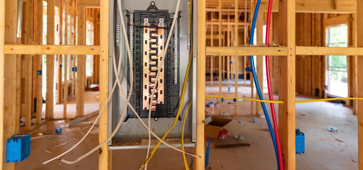 An electrical service panel and exposed wiring installed during a rough-in on a construction foundation.