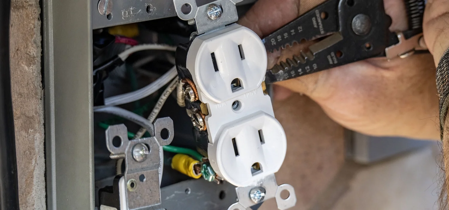 An electrician installing a wall socket while verifying the correct AWG wire size for the circuit's ampacity.
