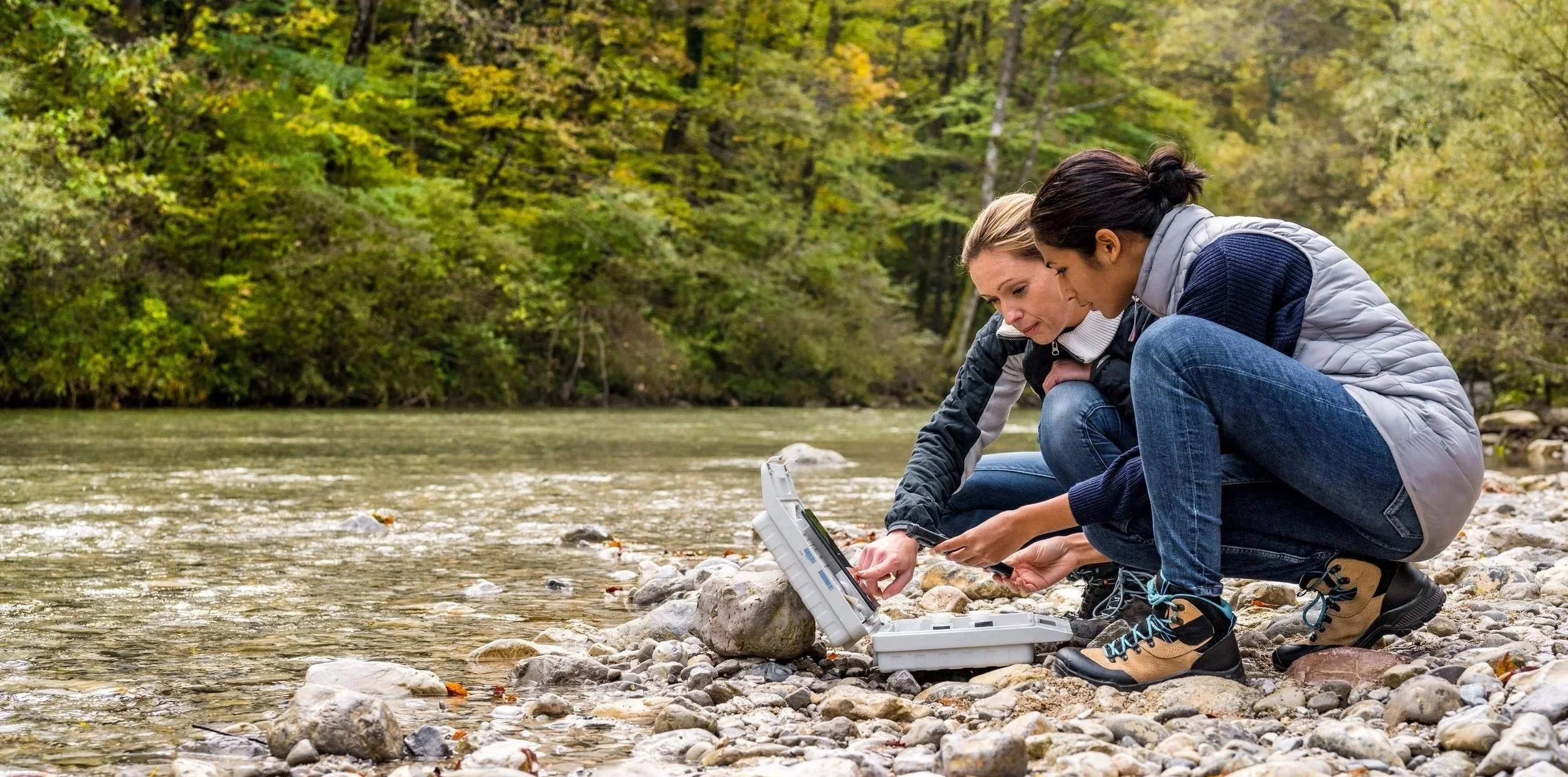 Two researchers collecting field data beside a forest stream — the kind of scientific work Computing for Humanity's research cloud supports.
