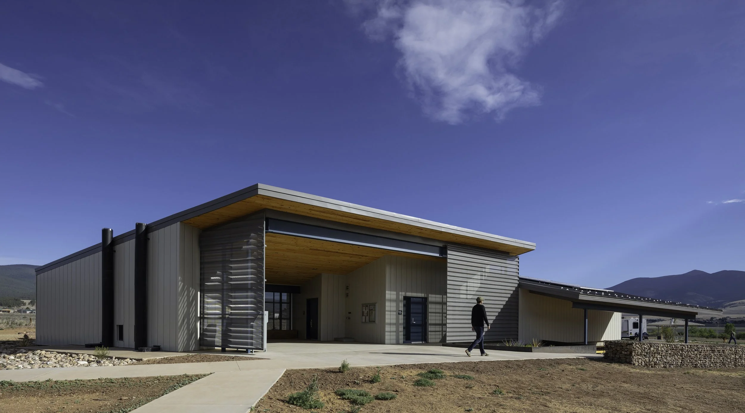 Comfort station featuring shaded overhang with man walking into restroom entrance