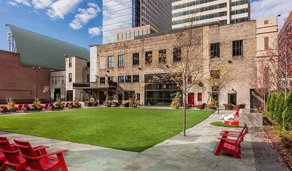An outdoor courtyard with green grass, red benches, and surrounding buildings in a city.