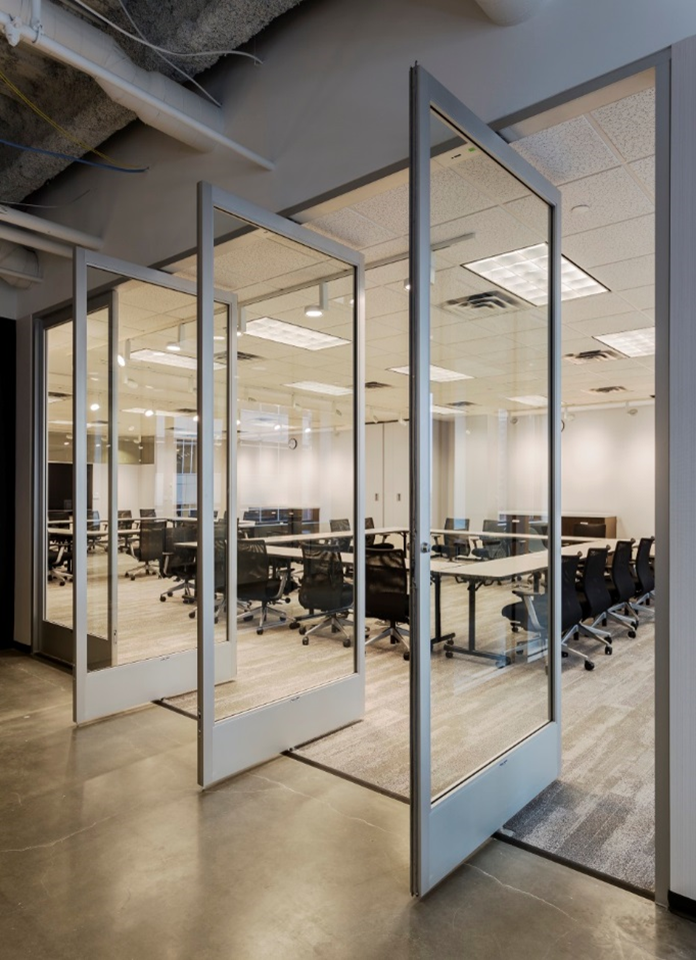 Empty modern conference room with glass walls and black ergonomic chairs around long white tables.