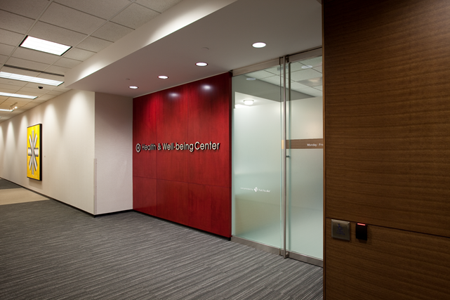 Interior view of a healthcare center with a red sign that reads 'Health & Well-being Center' and frosted glass doors.