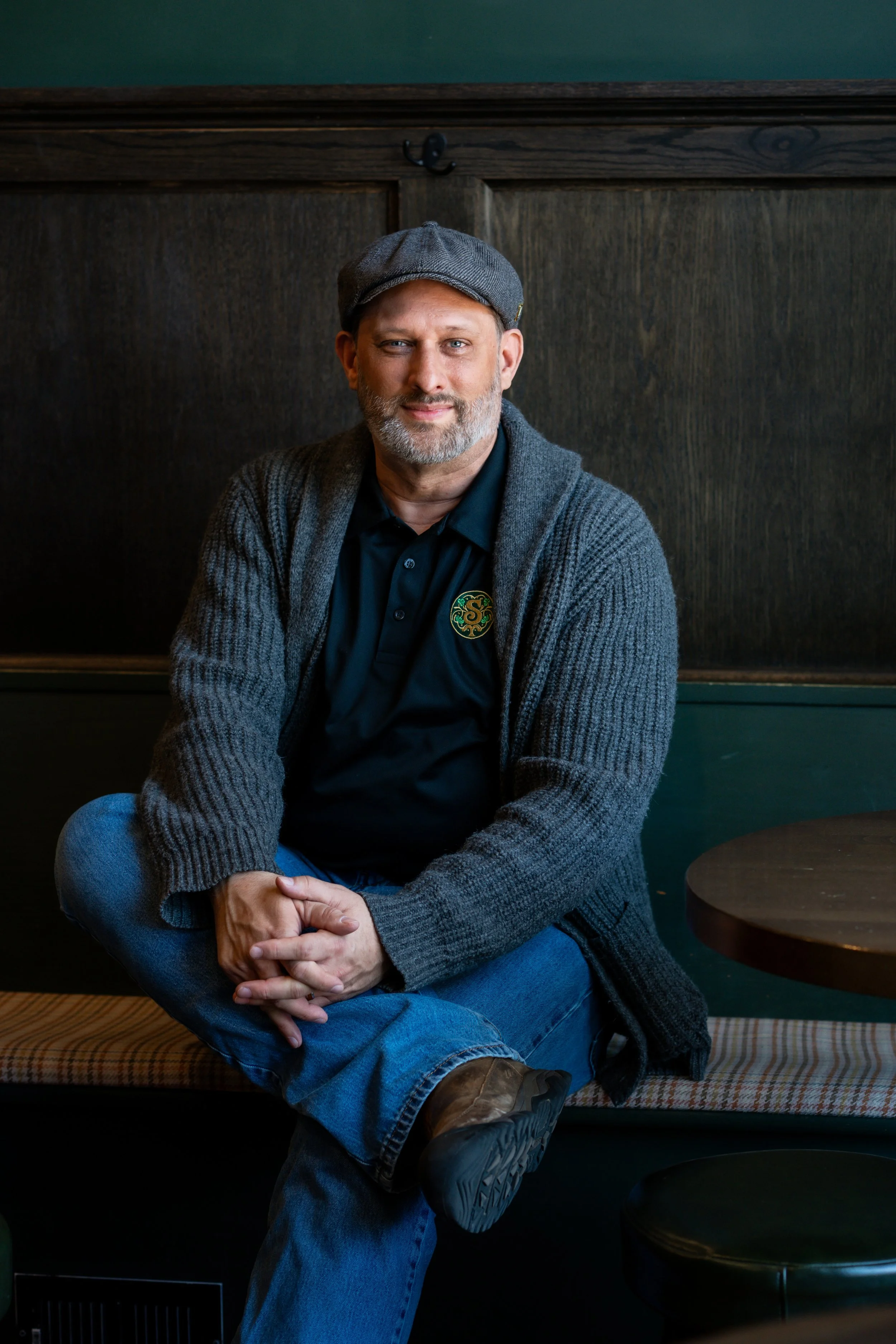 A man in a sweater with a flatcap on sitting on a bench