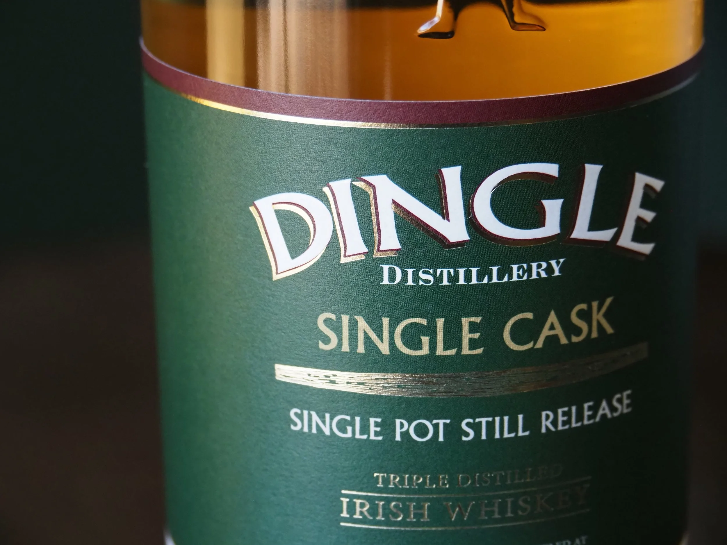 Close-up of a green and copper canister with the label 'Dingle Distillery Single Cask' and 'Single Pot Still Release' in white and gold lettering, indicating it contains Irish whiskey.