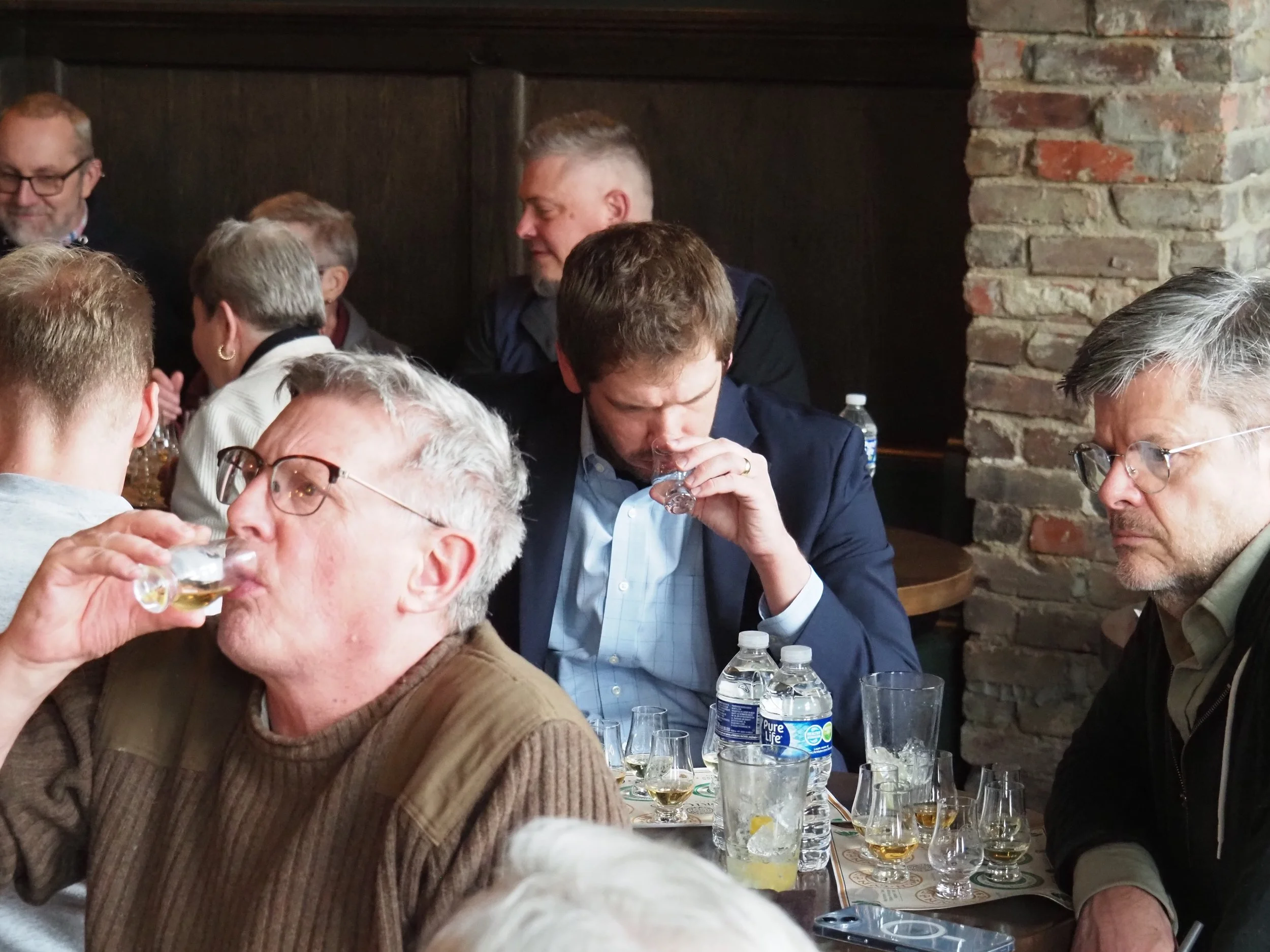 Several people seated around a table inside an Irish pub, with some drinking beverages, and water bottles and glasses visible on the table.