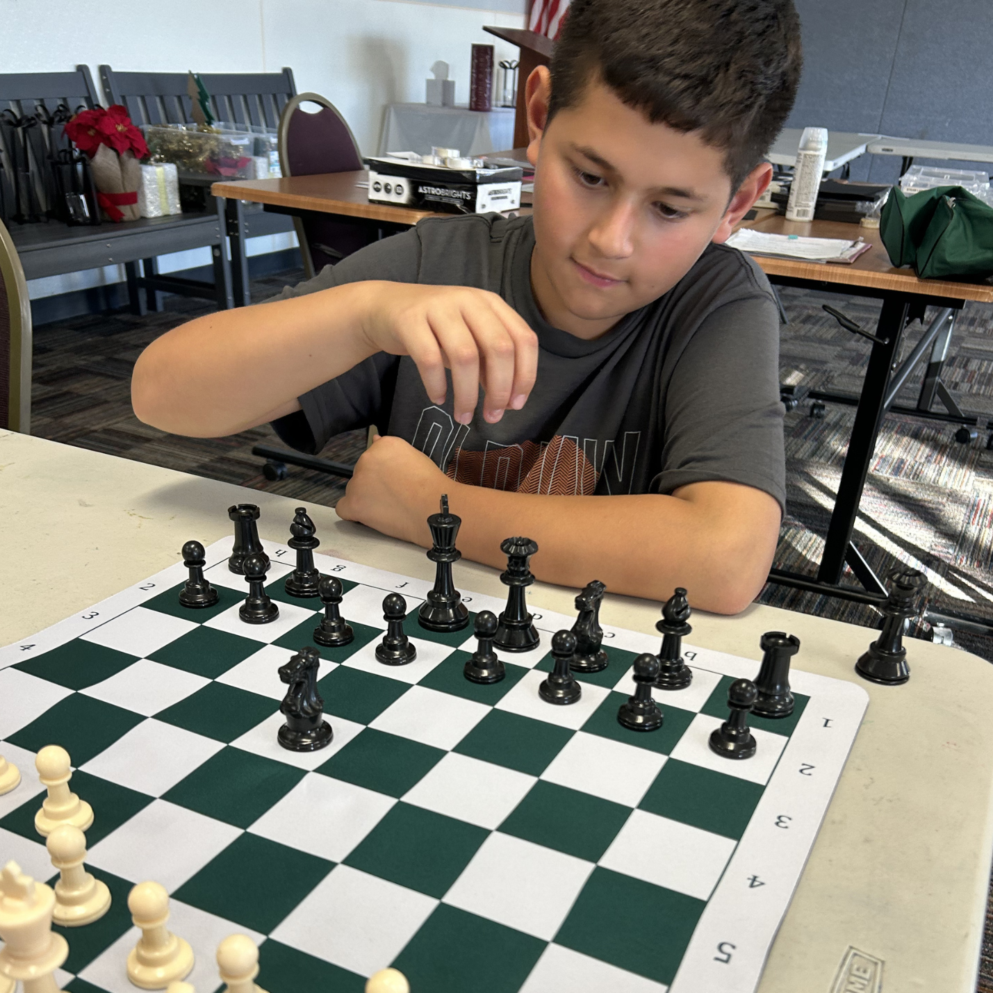 A young boy playing chess at a table, with a chessboard set up and pieces ready for a game.