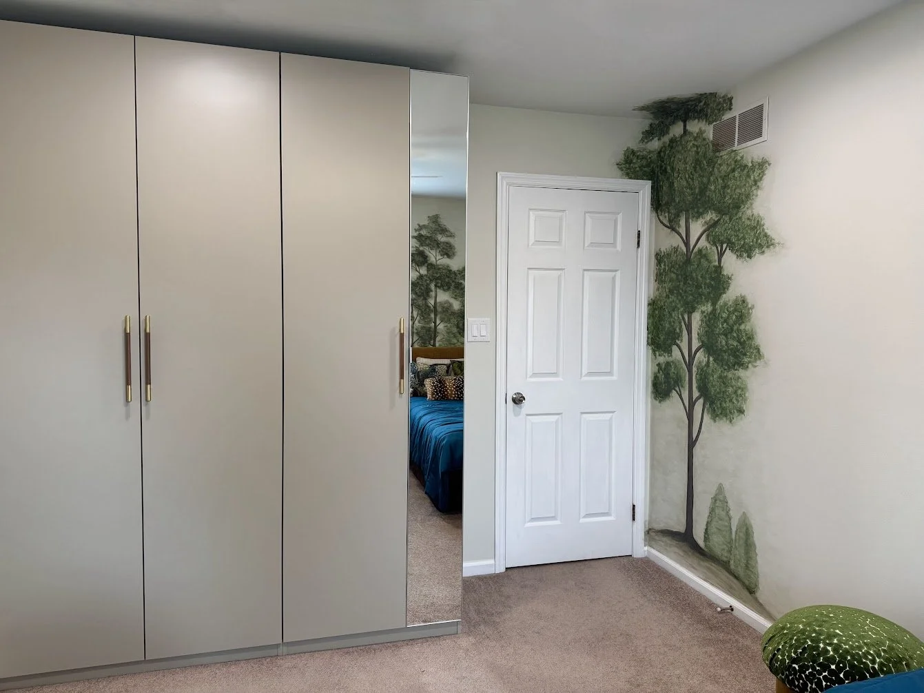 A wardrobe with a full-length mirror adds smart storage for guests while the forest mural continues seamlessly around the room.