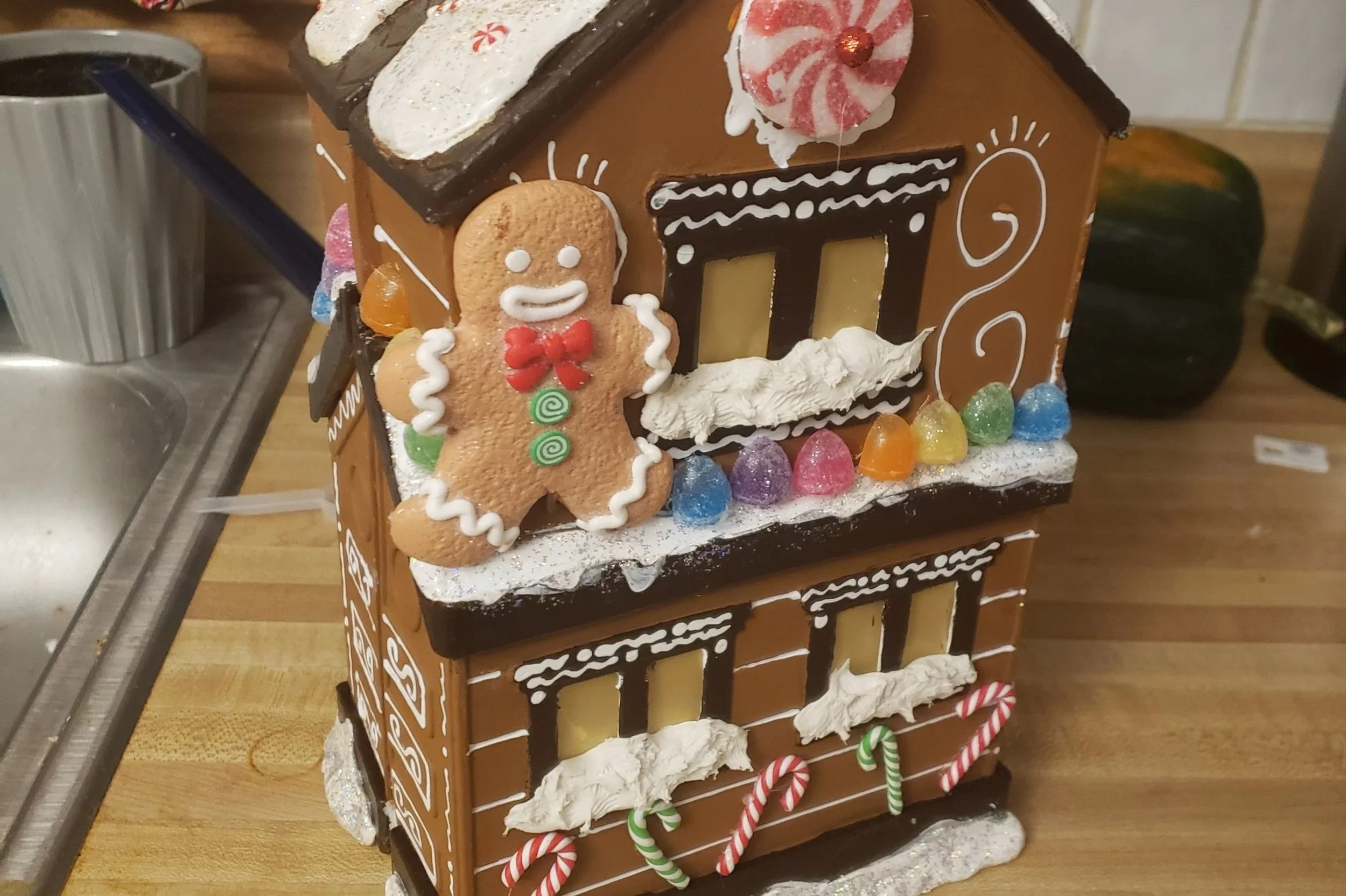 Decorated gingerbread house with icing and candy, featuring a gingerbread man and festive decorations.