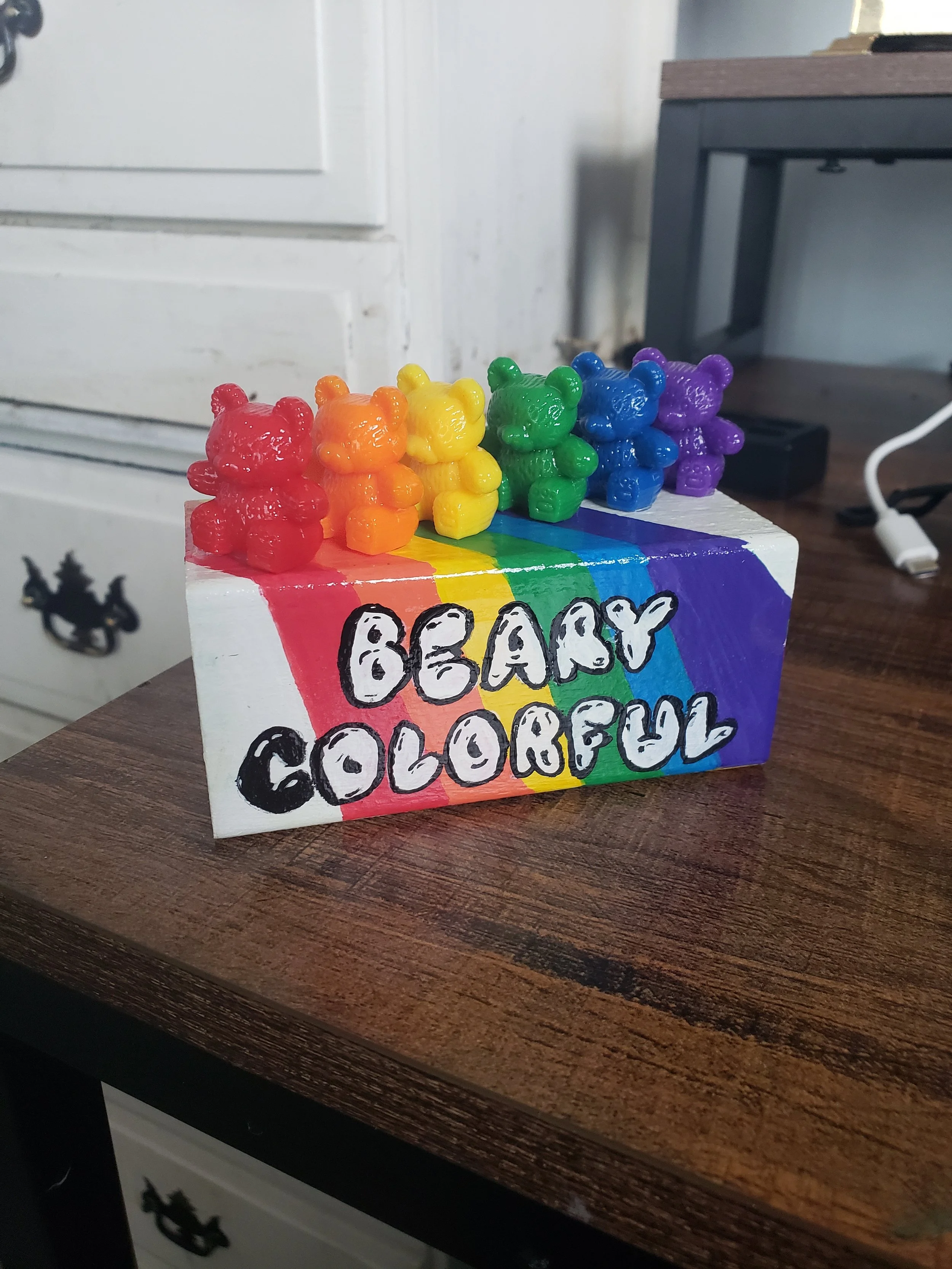Colorful painted block with the words "BE A LOVE, COLORFUL" and five small gummy bear figures in red, orange, yellow, green, blue, and purple on top.