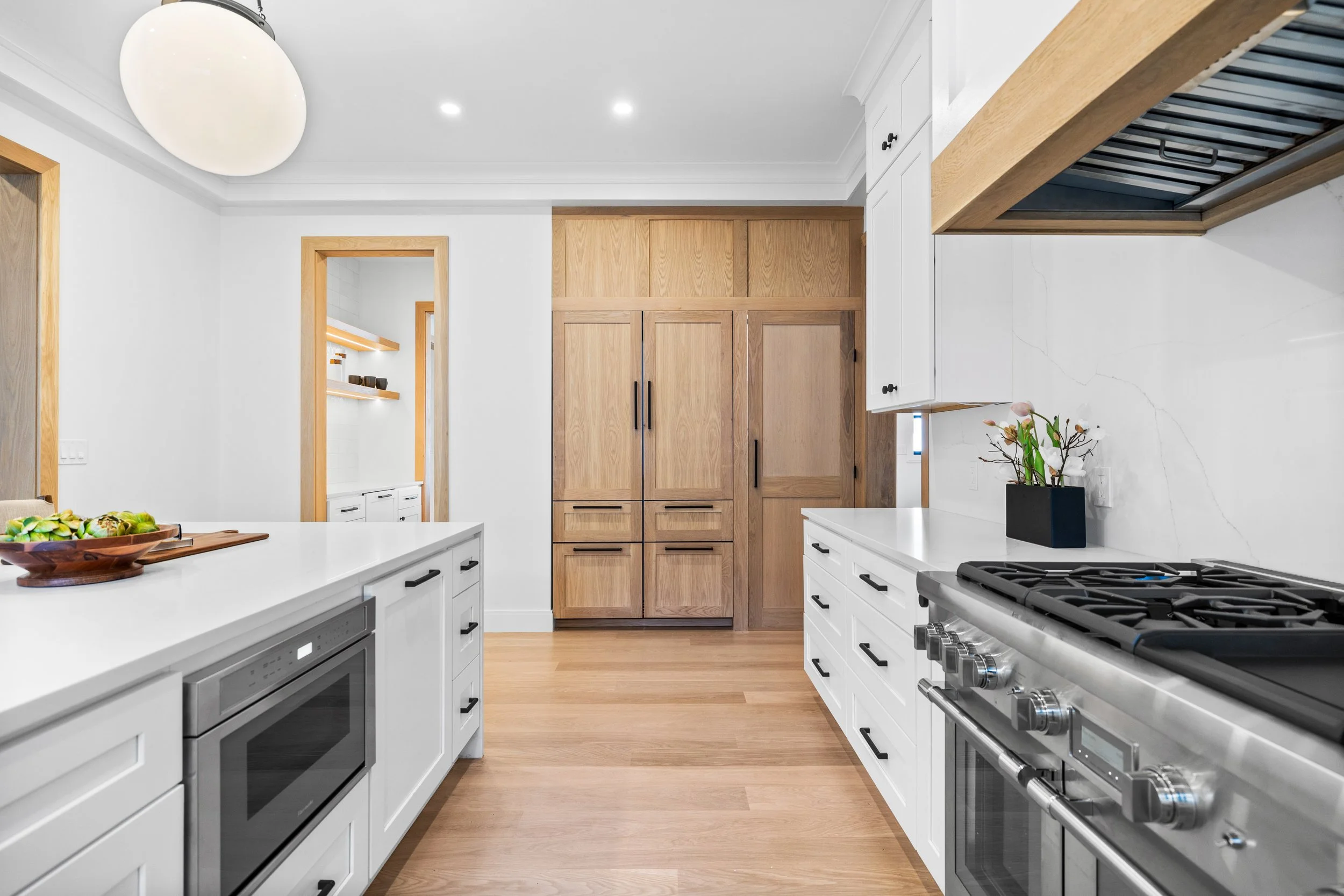 Modern kitchen with white cabinets, wooden accents, stainless steel appliances, and a black plant pot with flowers on the counter.