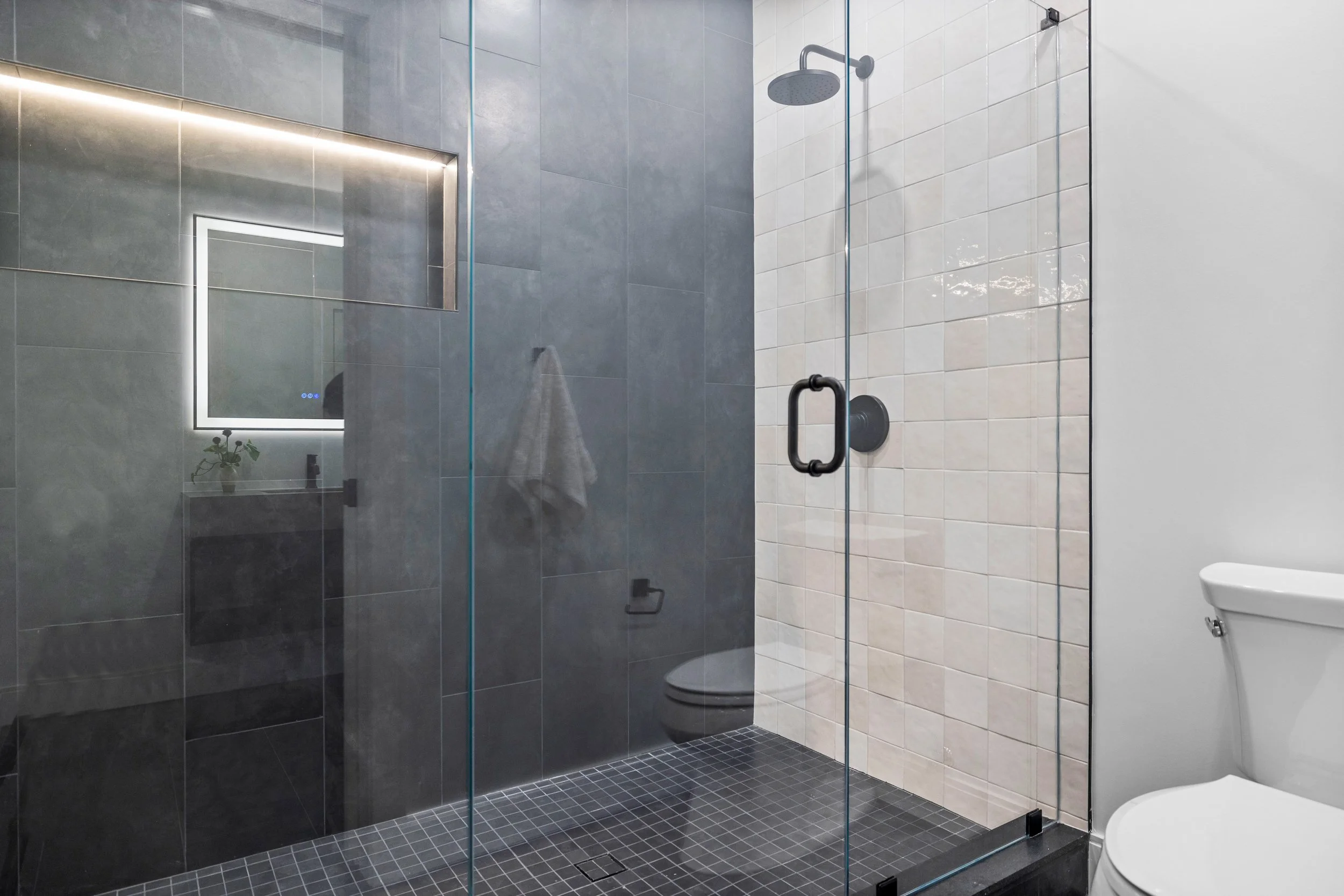 Modern bathroom with a glass shower enclosure, dark gray tiled walls, black fixtures, and a white toilet.