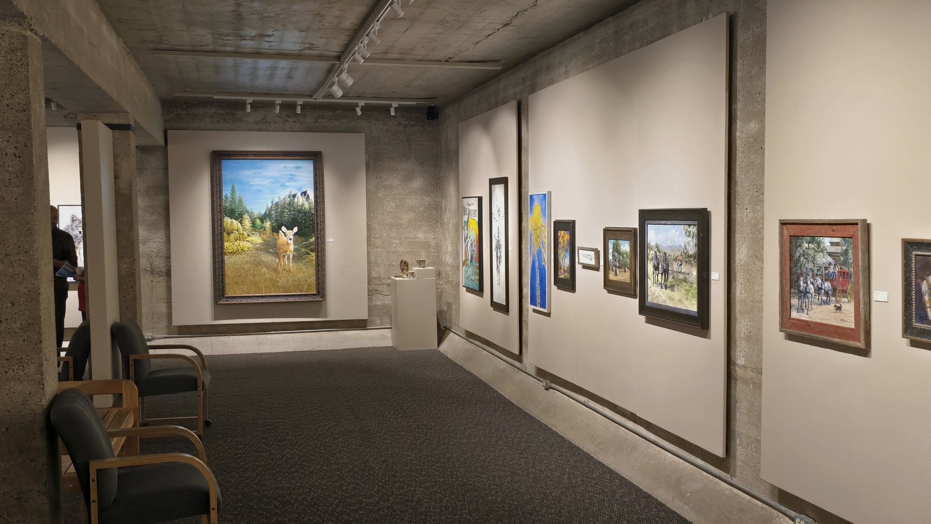 Waterworks Art Museum in Miles City, Montana with a large oil painting by Galen 'Mac' McAllister prominently displayed, along with other paintings, chairs and a carpeted floor.