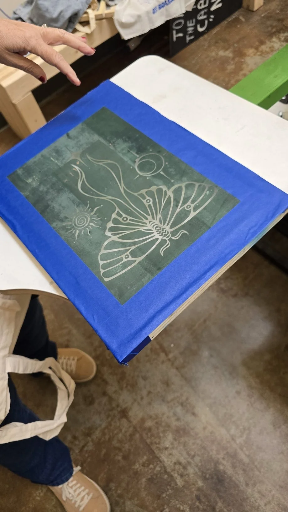 A decorated book or album featuring a butterfly, sun, and moon on a textured green background, bordered with blue paper, placed on a table.