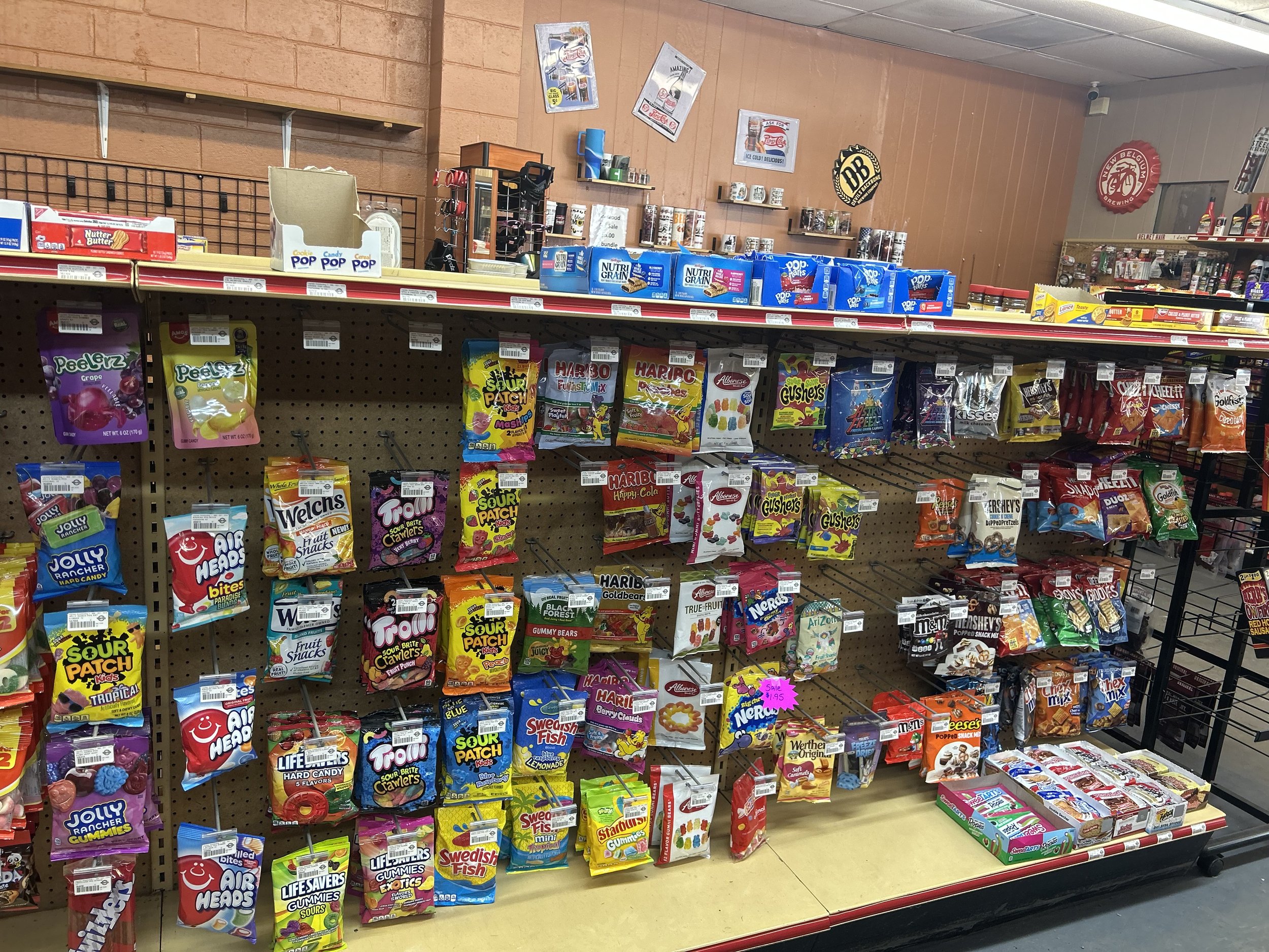Candy display shelf with various candy bags, including Gushers, Sour Patch Kids, Air Heads, Swedish Fish, and Reese's in a store aisle.
