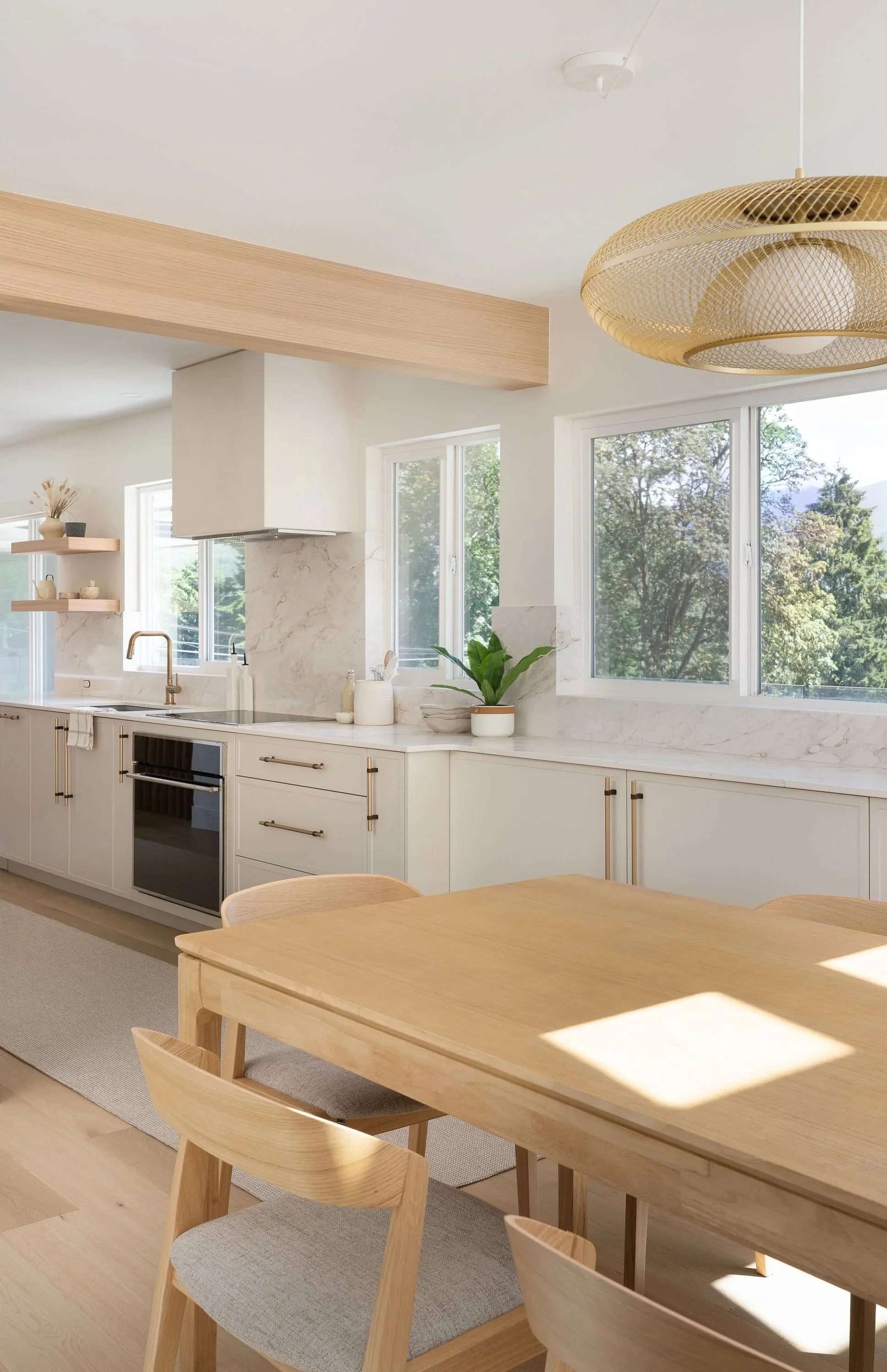 Bright kitchen with white marble backsplash, cream cabinetry and brushed brass fixtures, interior design by Emilija Matas Design