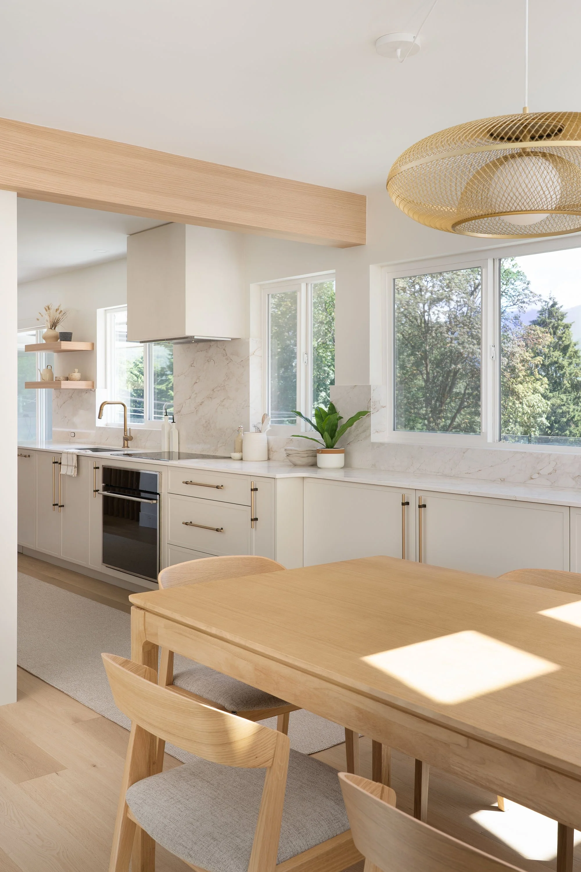 Modern kitchen with white cabinets, marble countertops, large windows, and wooden dining table with matching chairs.