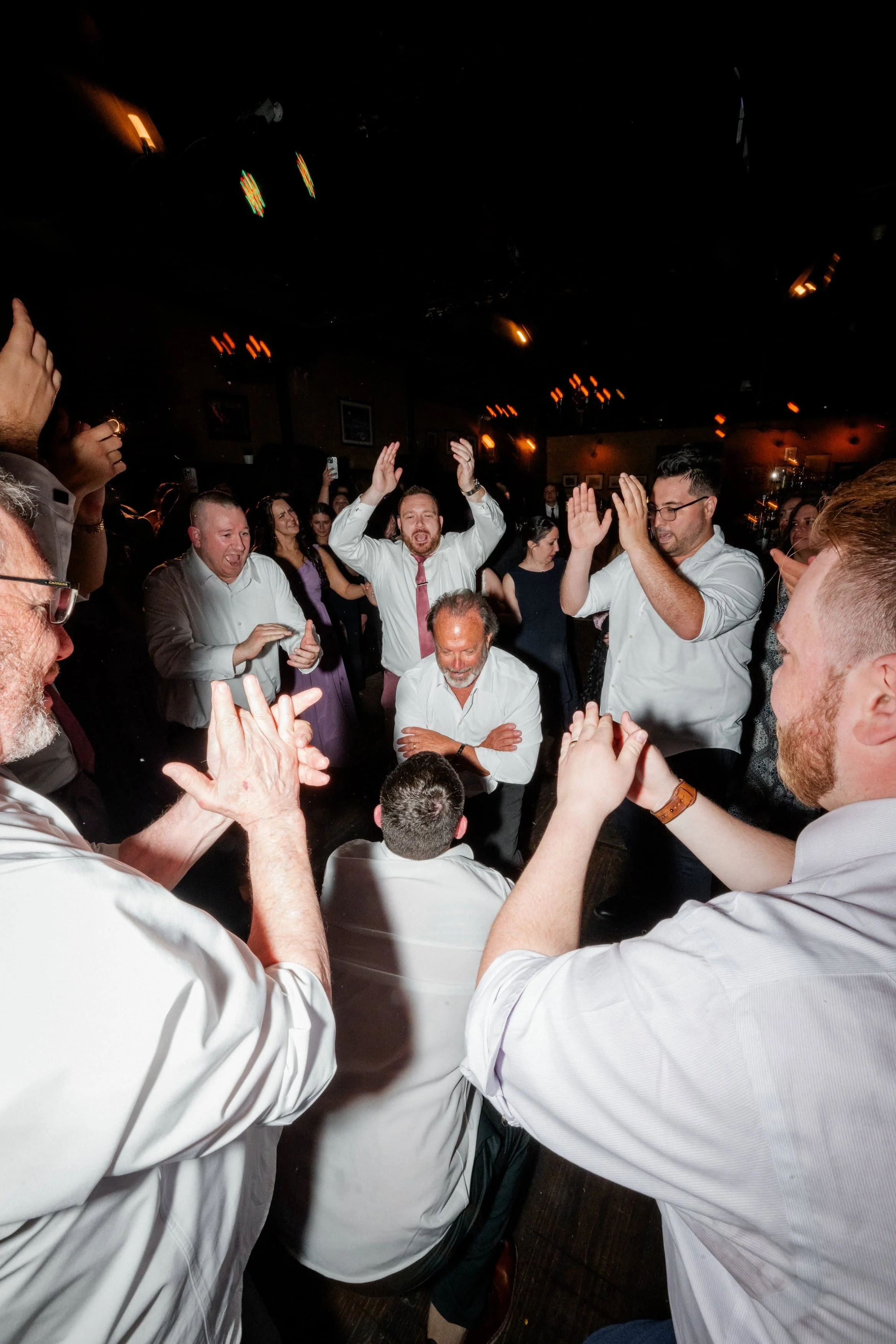 People dancing and celebrating at a party or wedding reception in a dimly lit venue.