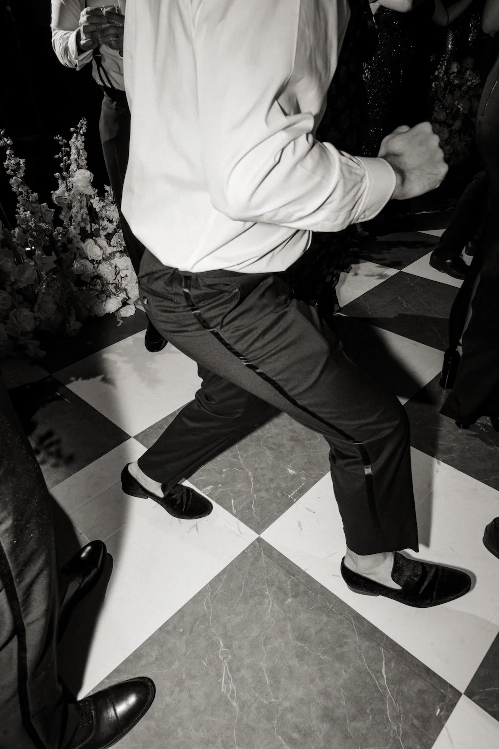Person in white shirt and dark pants dancing on checkered floor at a social gathering.