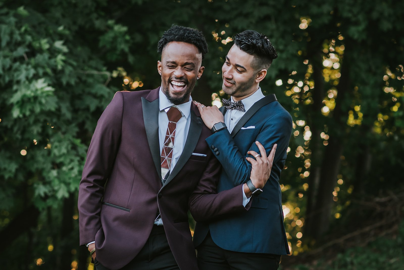 Two men dressed in formal suits laughing together outdoors during daytime.
