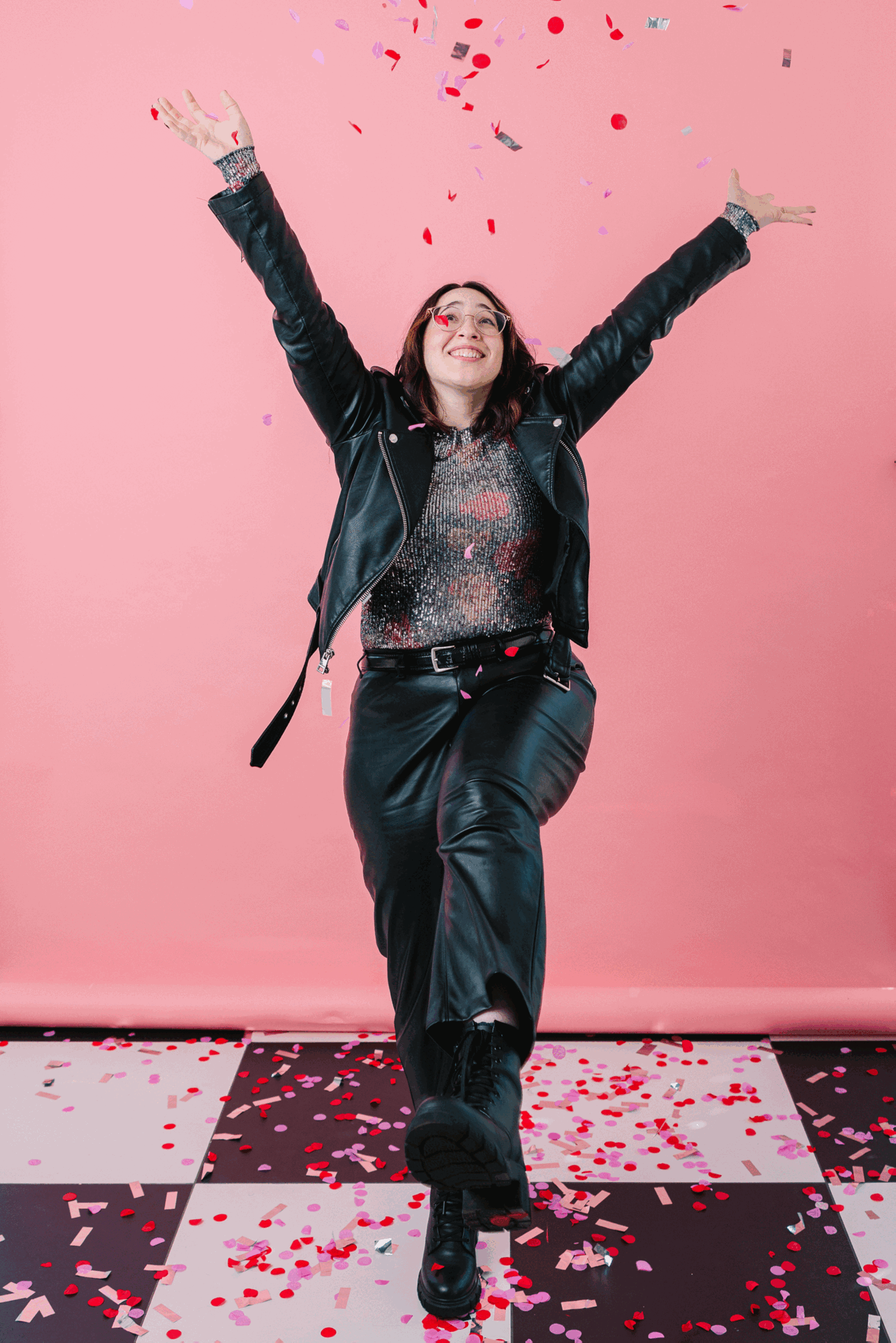 michelle chriqui hidalgo throwing confetti wearing a sparkle shirt and leather outfit in front of a pink wall.
