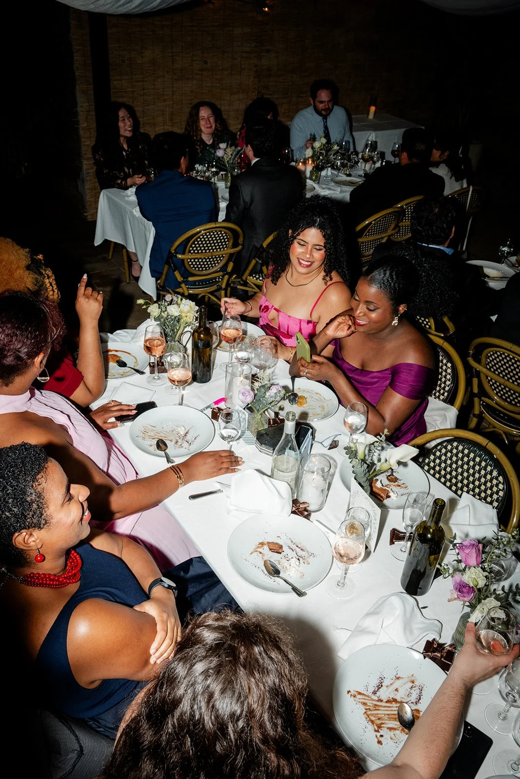 People enjoying a dinner party at a long banquet table with plates, glasses, and floral centerpieces.