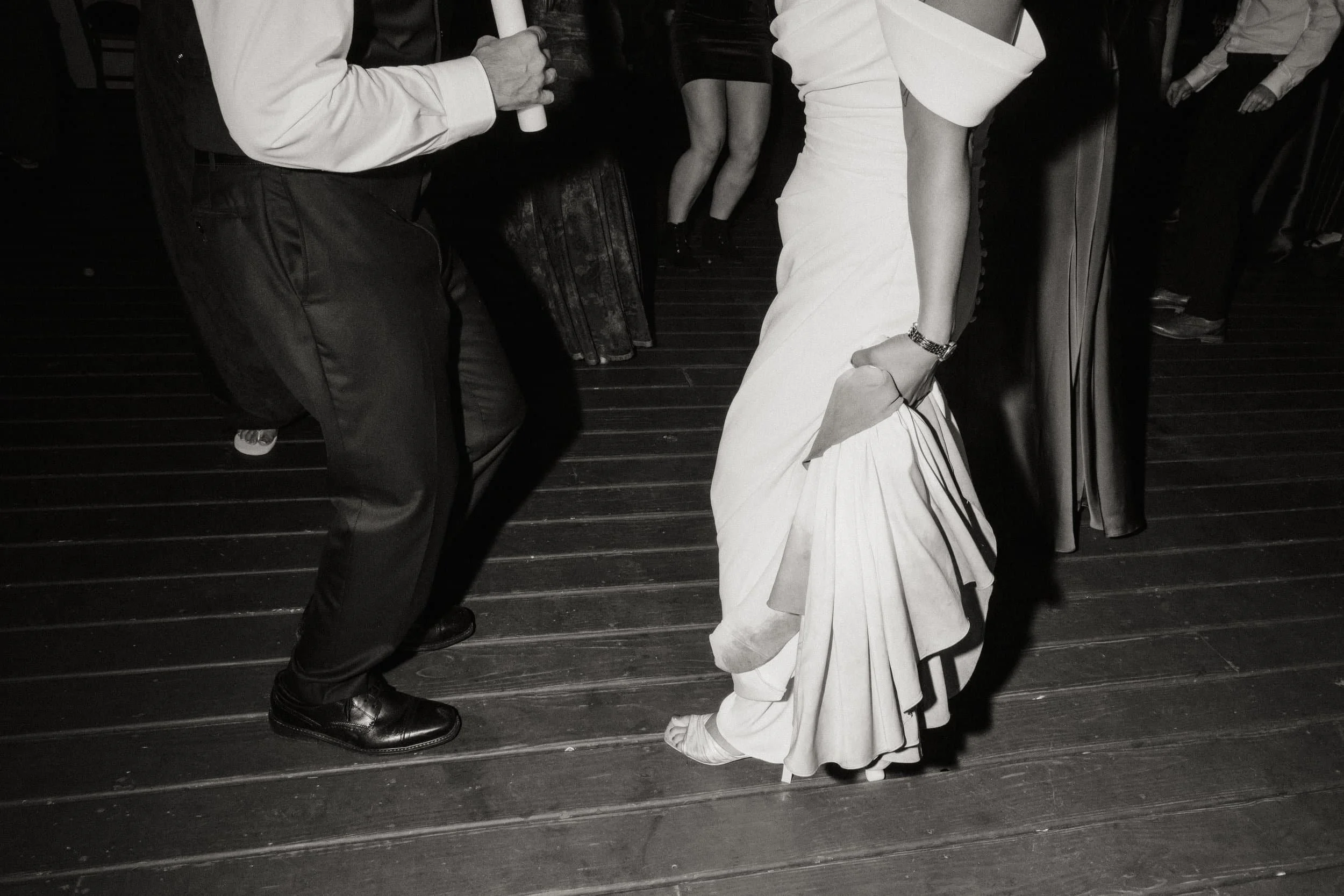 People dancing at a social gathering, with focus on a woman in a white dress and another person in dark clothing.
