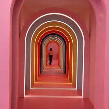 A person standing under a series of colorful archways with pink walls, creating a tunnel effect.
