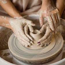 Hands shaping clay on a pottery wheel during a pottery-making activity.