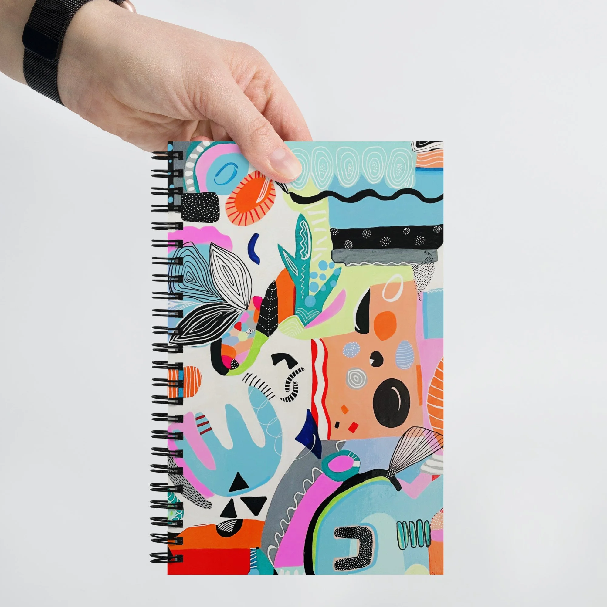 hand holding a spiral notebook with colorful "synchronicity" art applied to the cover