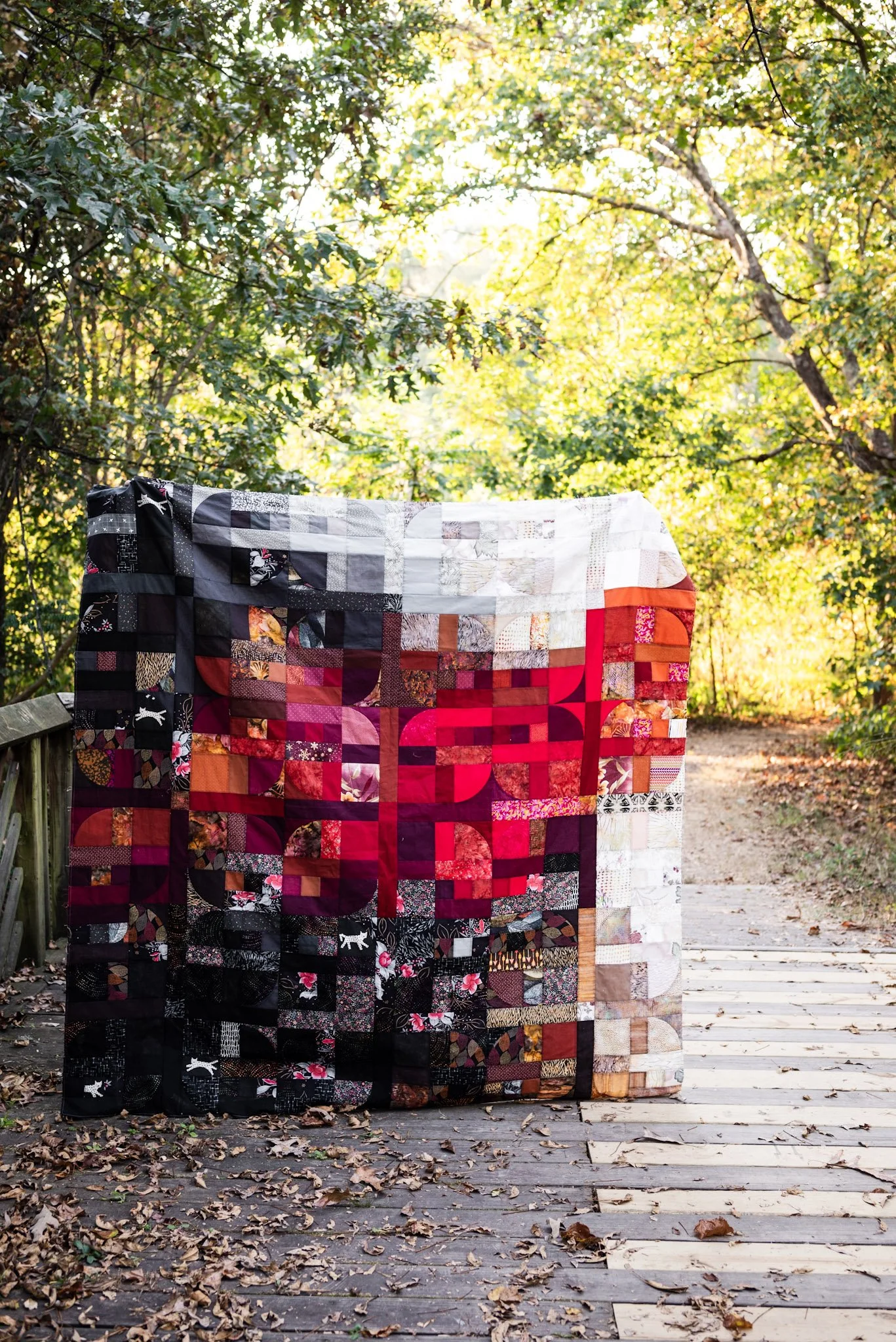 A red, black and white quilt in an autumn forest on a wooden bridge