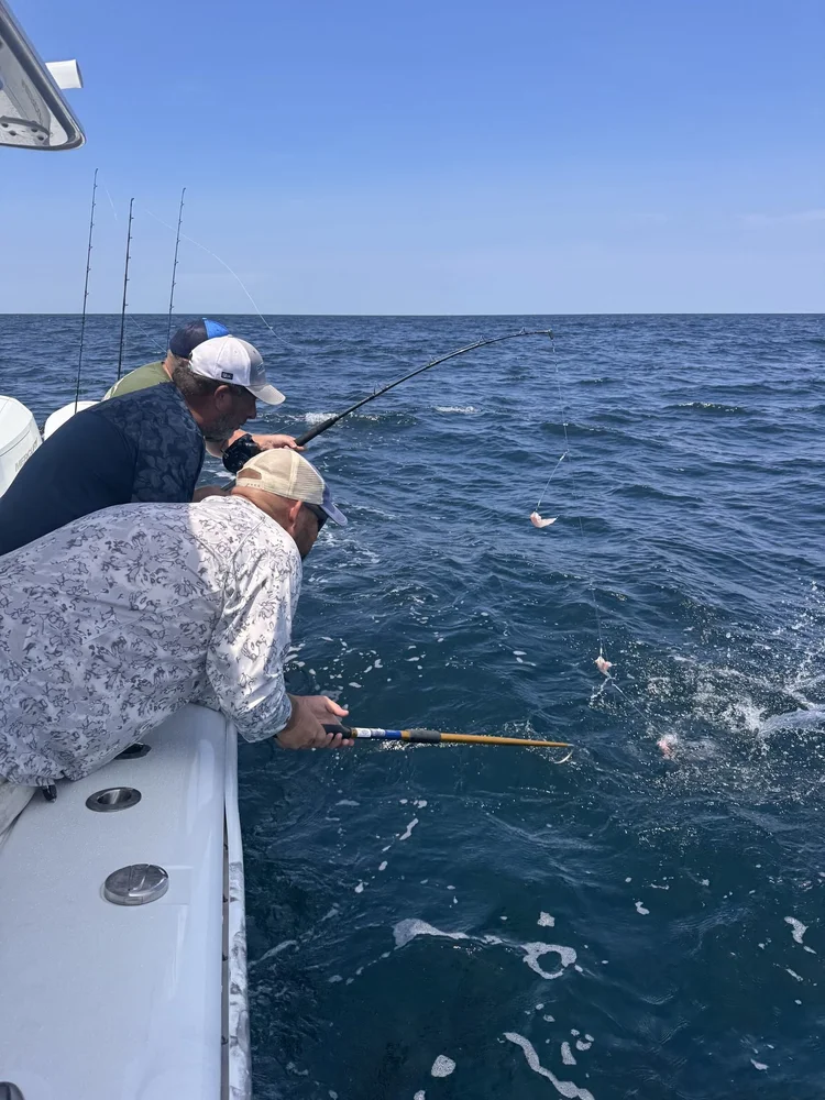 Two anglers working a fish at the rail in blue water