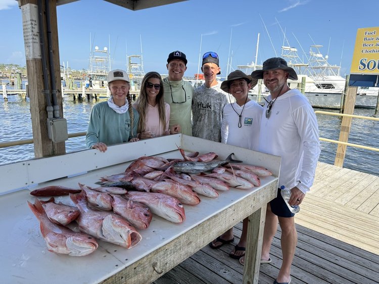 Six anglers behind a full cleaning table at the dock
