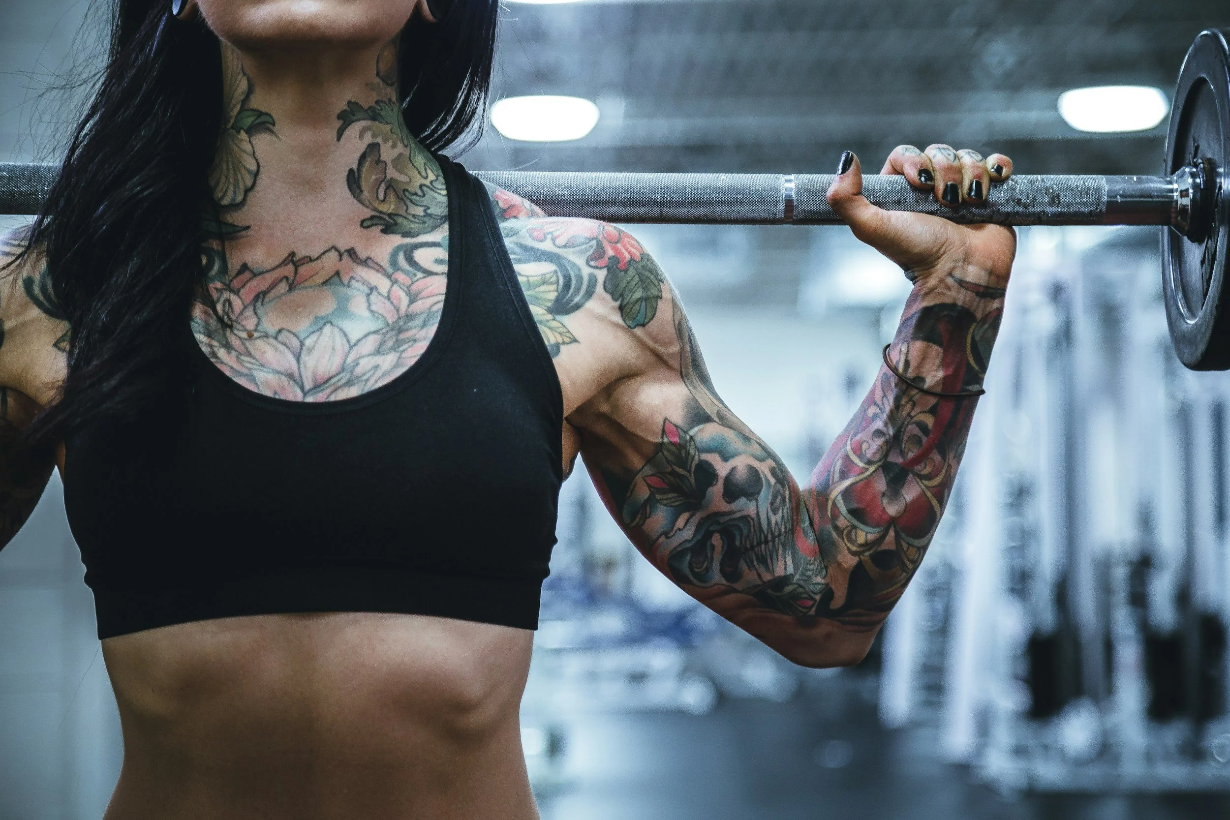 A tattooed woman lifting a barbell in a gym.
