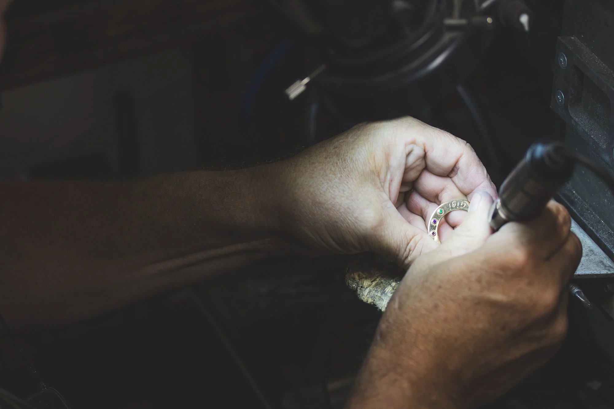 Person holding and working on a metal ring or jewelry piece with a tool, in a workshop setting.