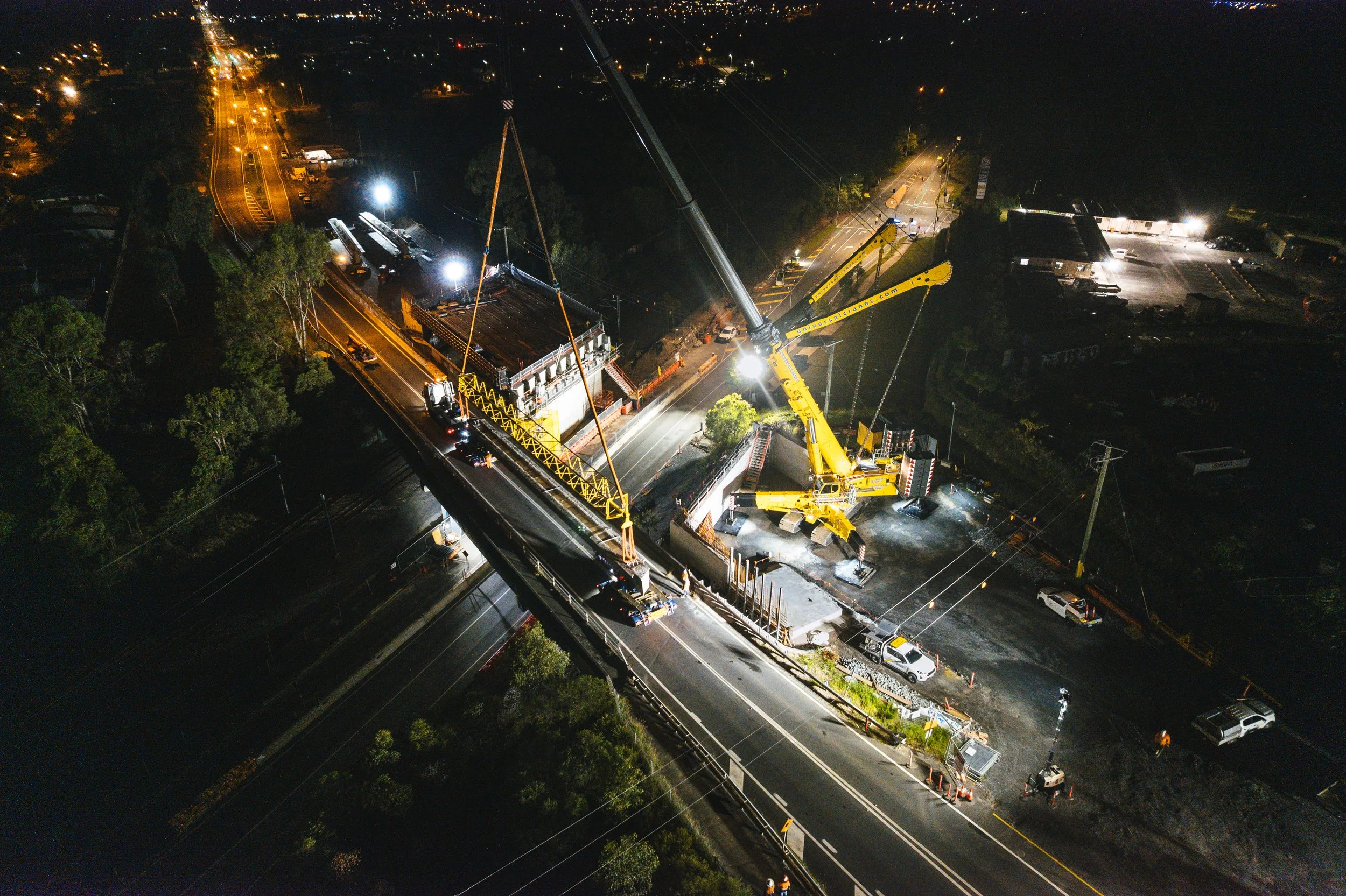 Modern wooden house with a large glass window, surrounded by yellowish shrubs and mountains in the background.