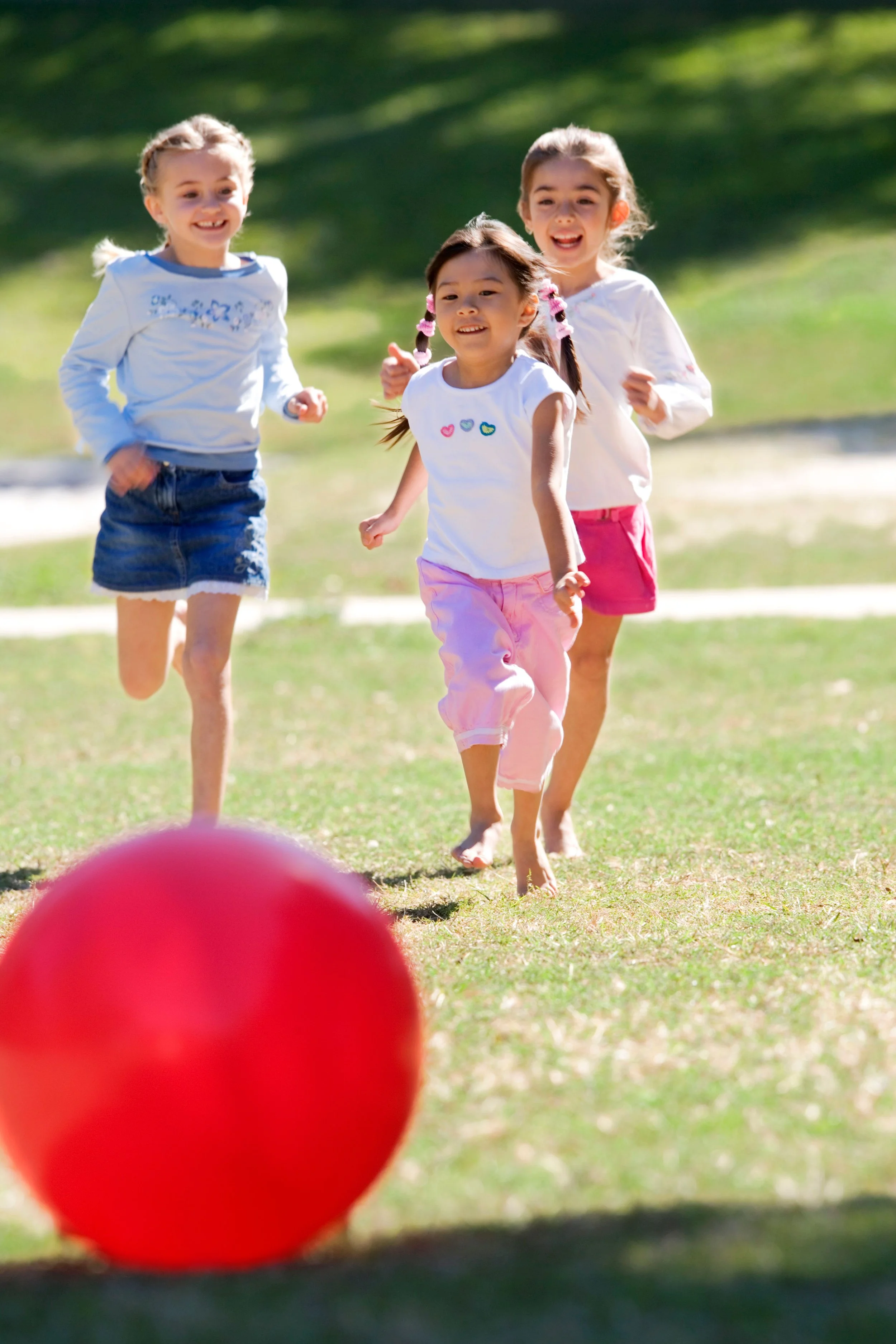 Three girls chasing a big red ball and smiling
