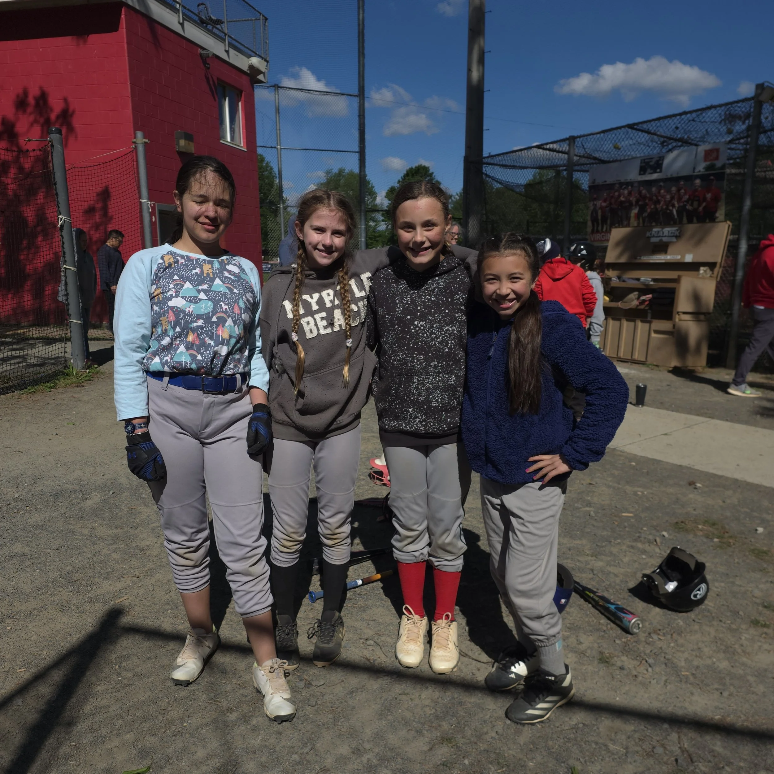 Four D.C. Girls Baseball Players stand together outside near their practice field.