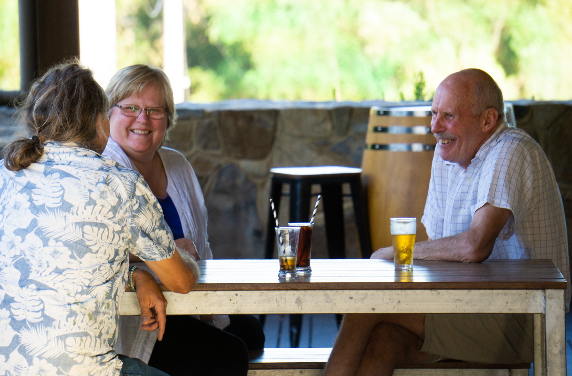 Three smiling people sitting around a bar table with drinks, engaged in conversation.