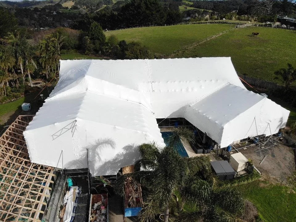 An aerial view of large white temporary shrink wrap covering a residential property with trees, a pool, and surrounding greenery.