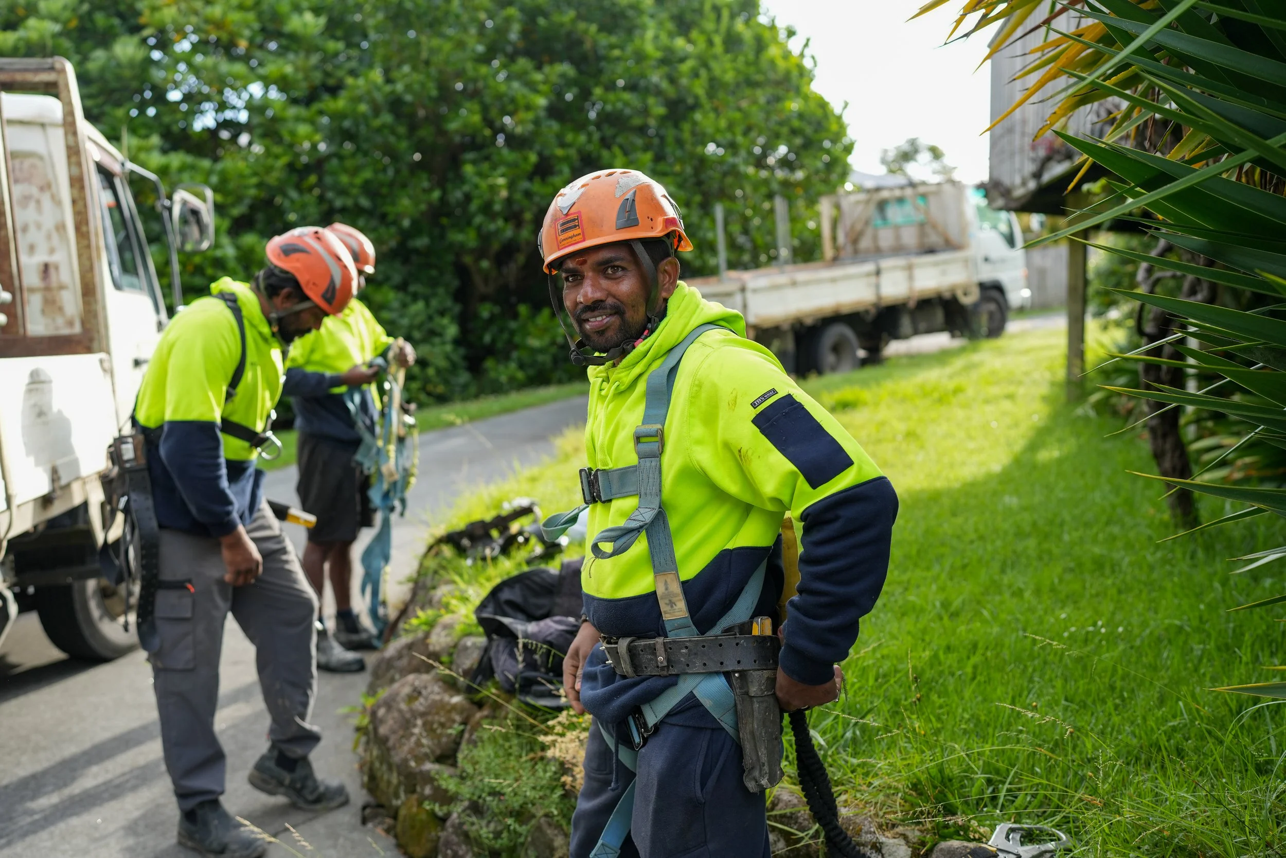 Smiling scaffolder standing by his team and a truck and putting on a safety harness