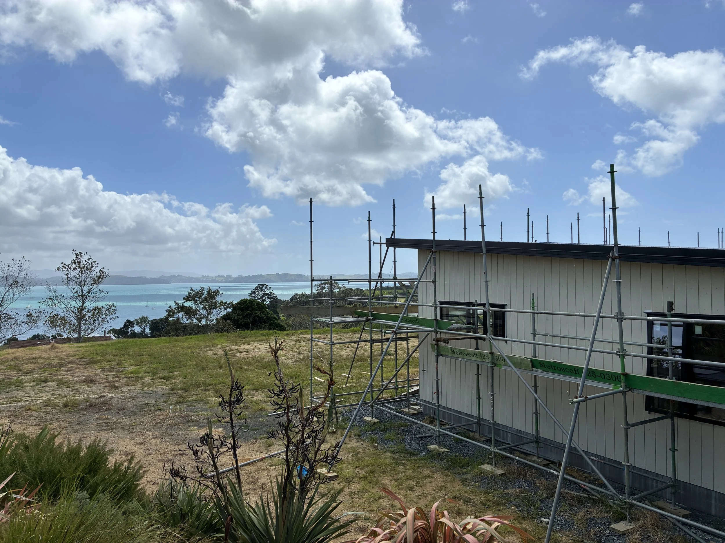 Scaffolding in front of a home with a view of the ocean and a partly cloudy sky in the background.