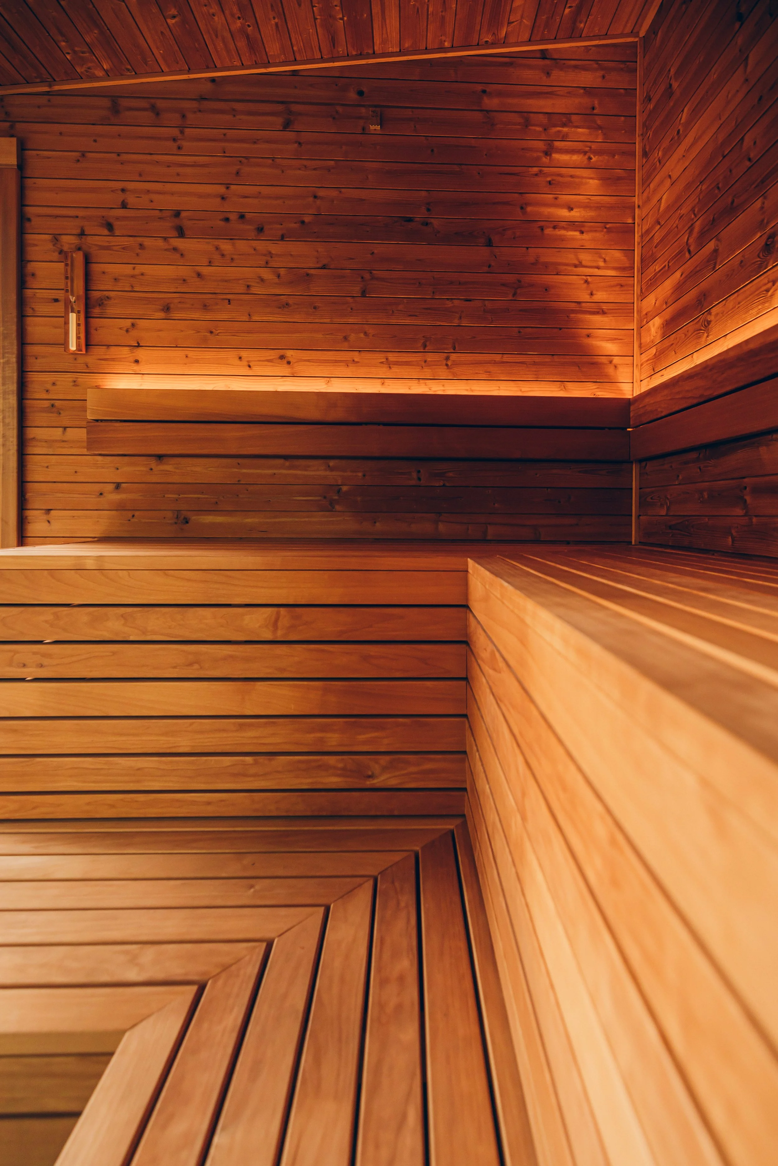 Interior of a wooden sauna with horizontal and vertical wooden planks, warm lighting, and a wooden bench.