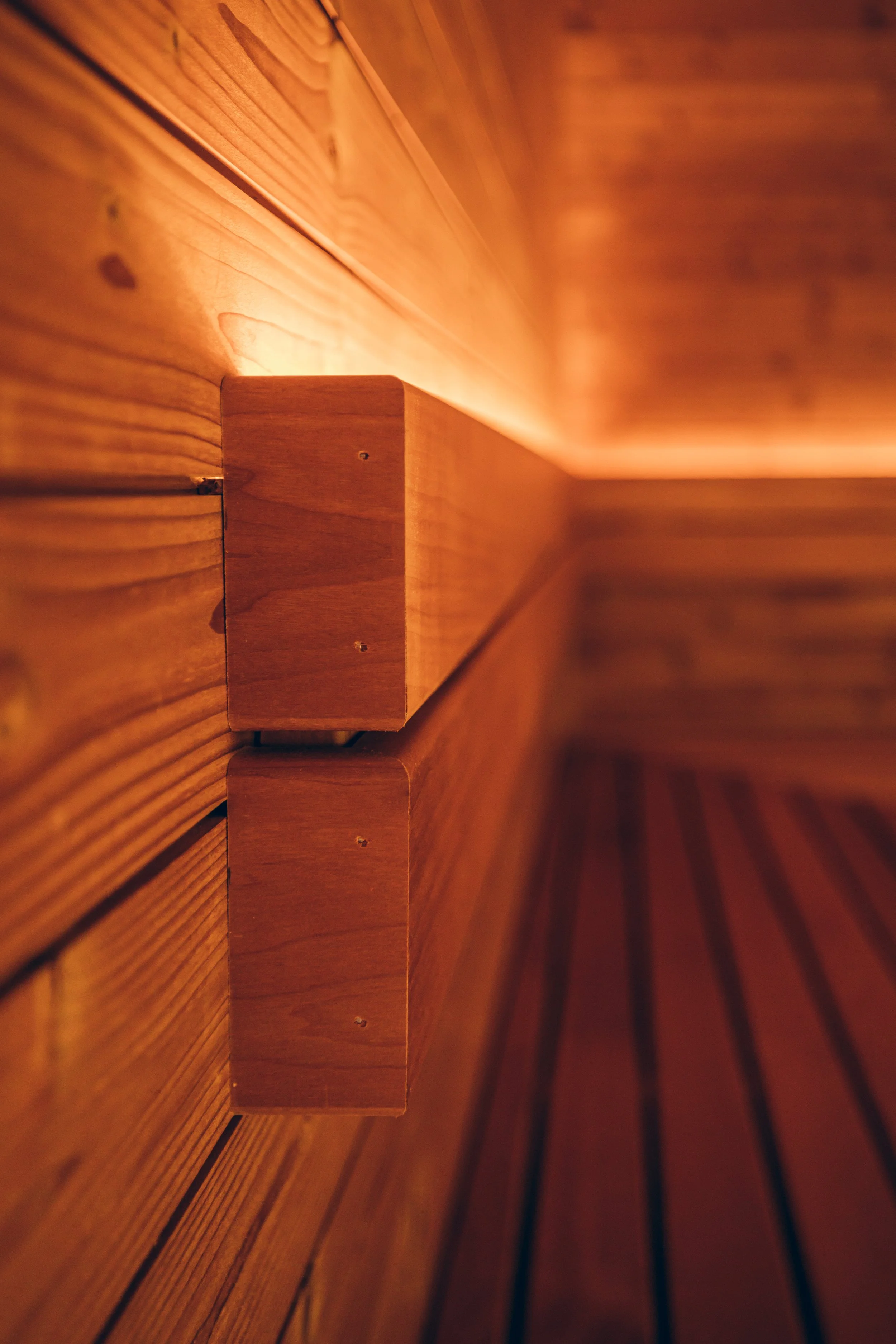 Close-up of wooden wall with a horizontal wooden block attached, showing warm lighting highlighting the wood grain.