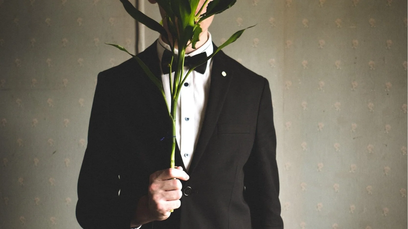 A mysterious man in a suit hiding his face behind a bunch of roses