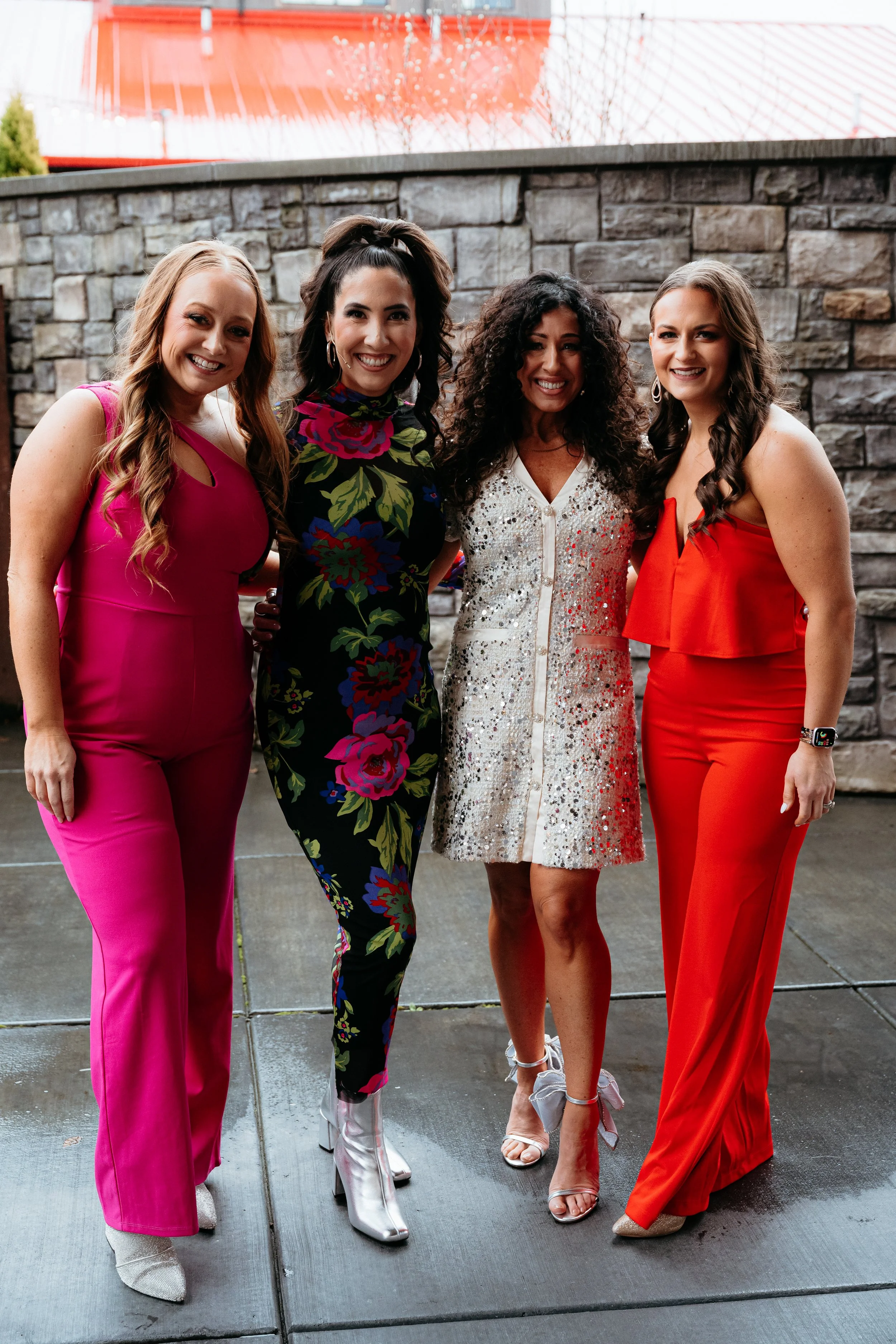 Four women dressed in colorful outfits smiling outdoors.